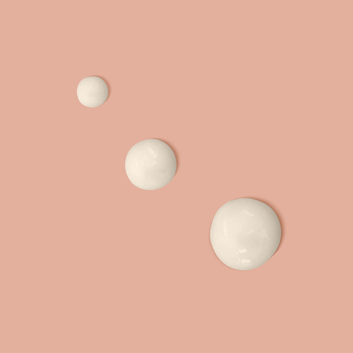 Three drops of face tan cream on peach coloured background