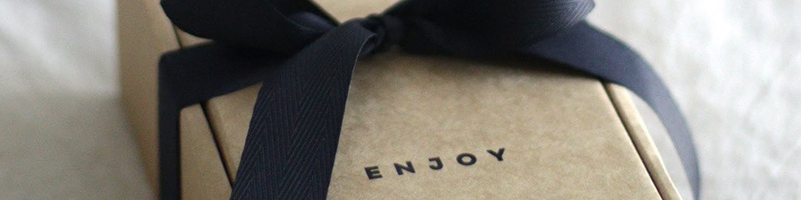 Beautiful kraft paper gift box on linen bedding with printed text 'enjoy' and a black ribbon