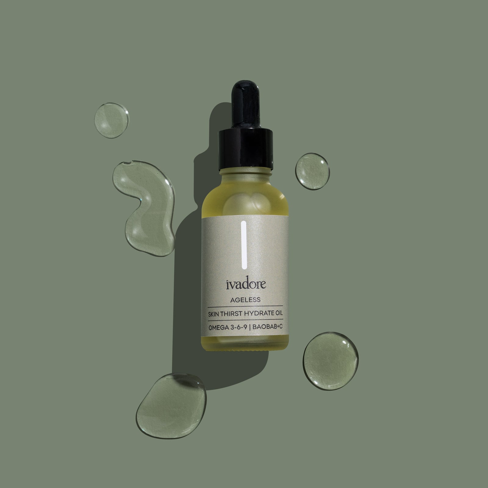 Flatlay view of Ivadore Ageless face oil surrounded by clear oil droplets