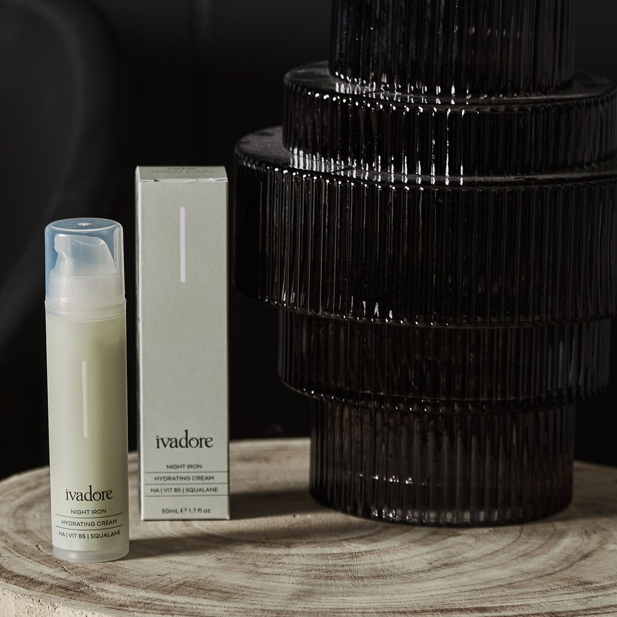Night Iron Hydrating Cream in packaging on wooden table with grey glass vase