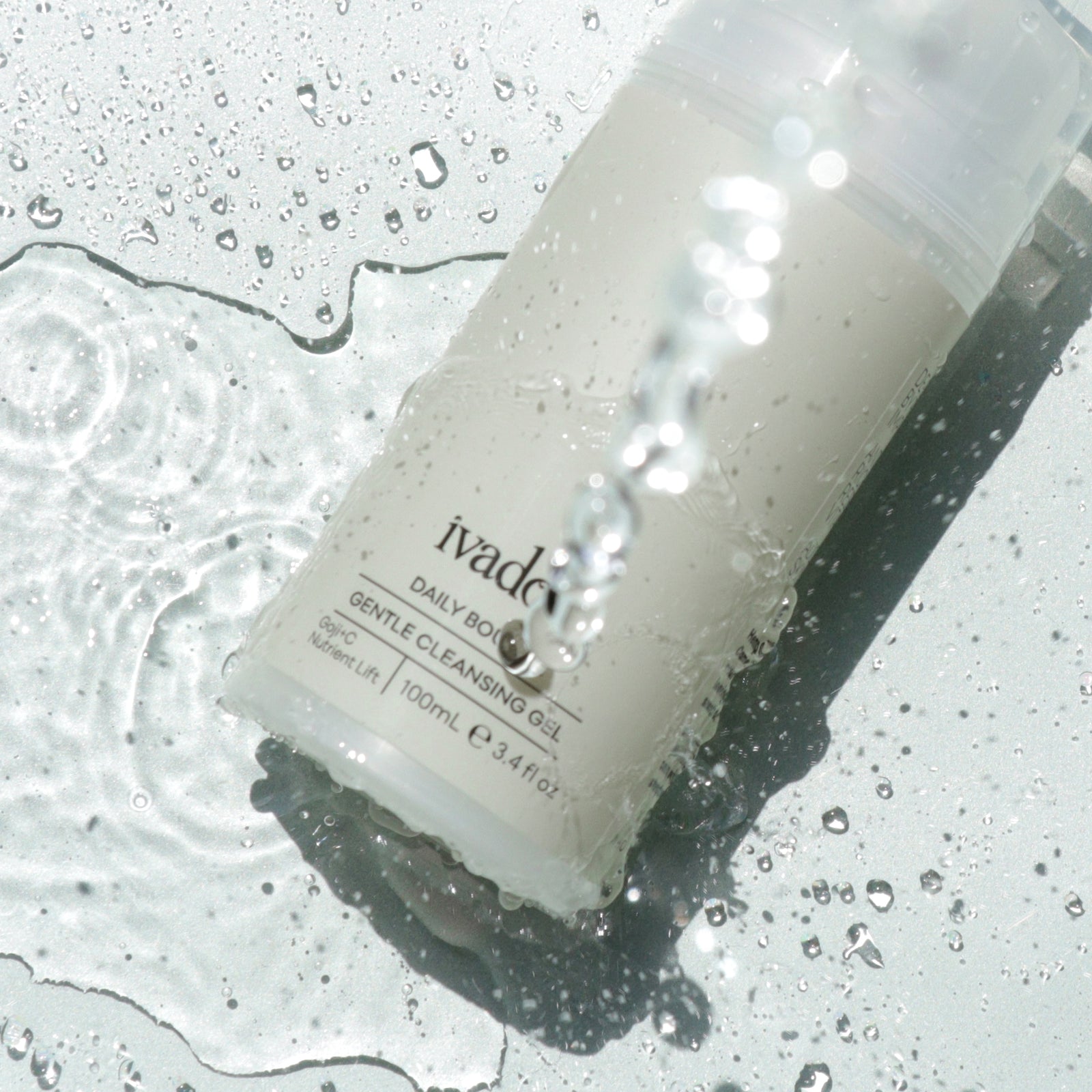 Photograph showing Daily Bounce Cleansing Gel bottle on mint green background with water splashing over it