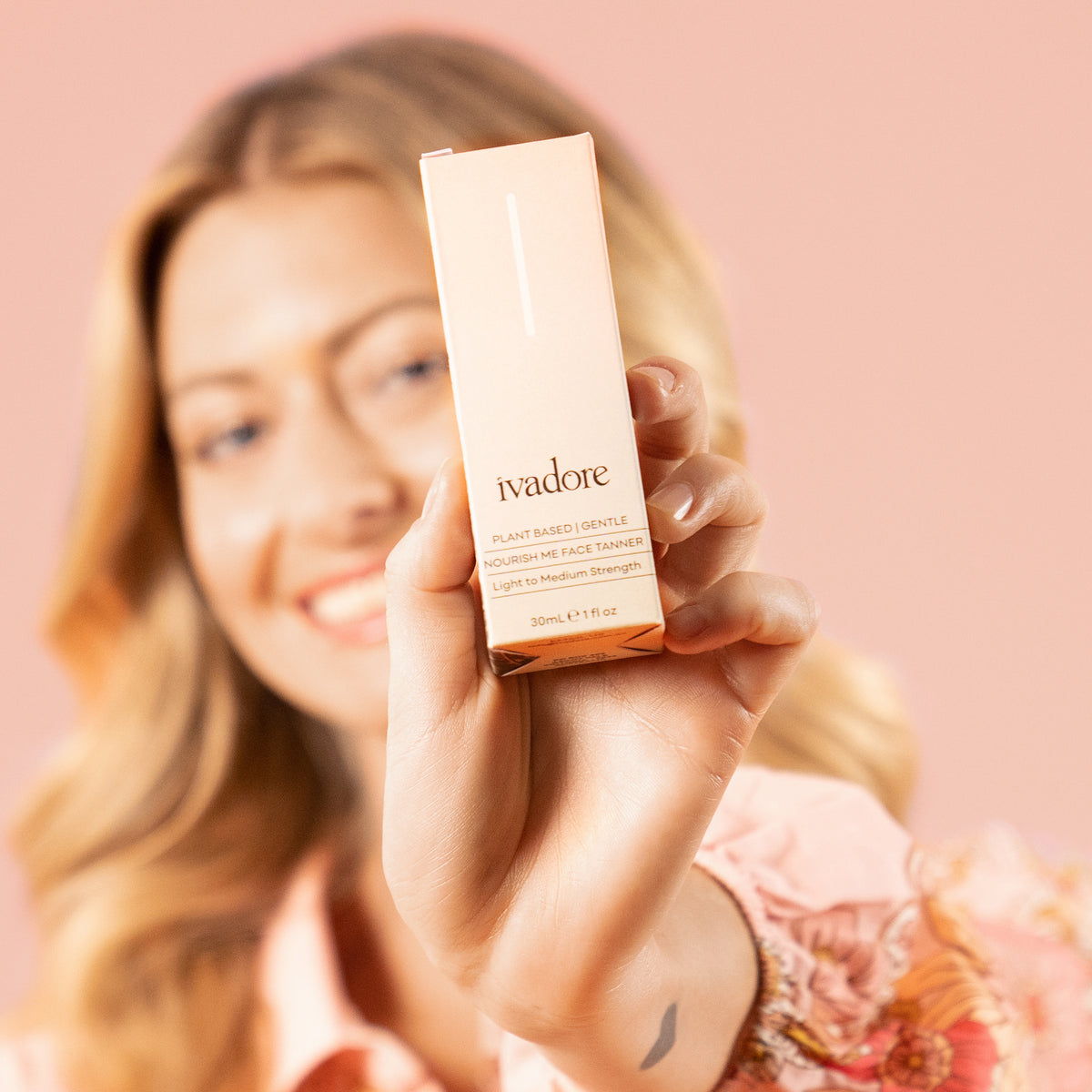 Smiling woman with blonde wavy hair holding Ivadore face tan box  to camera