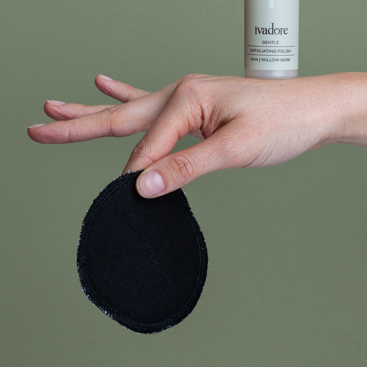 Female hand holding black washable facey wipe balancing a gentle exfoliating polish on top of hand