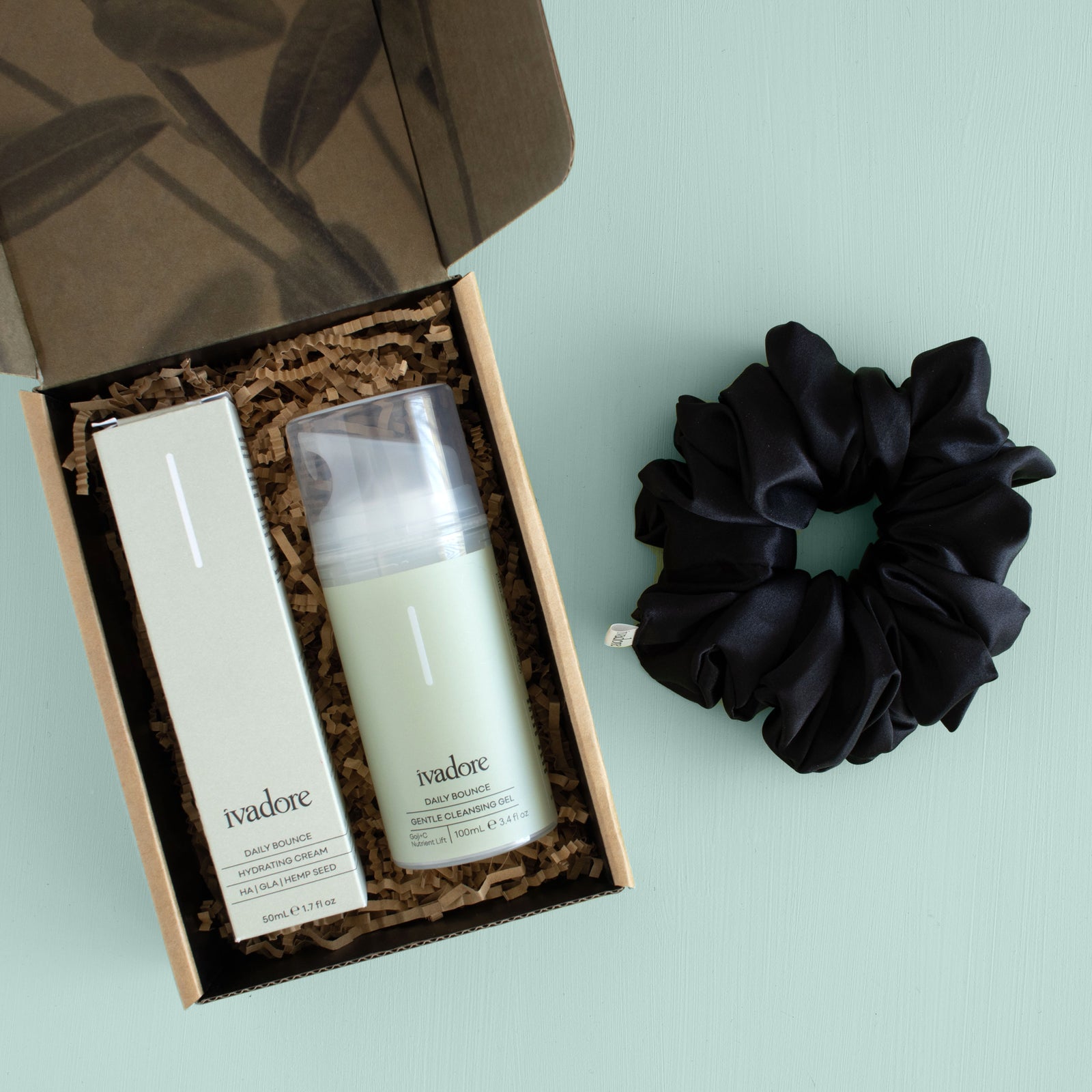 Printed gift box with face cleanser and face moisturiser inside, black silk scrunchie next to set