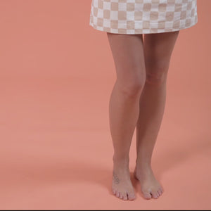 Female wearing white denim skirt applying moisturising self tan cream to legs