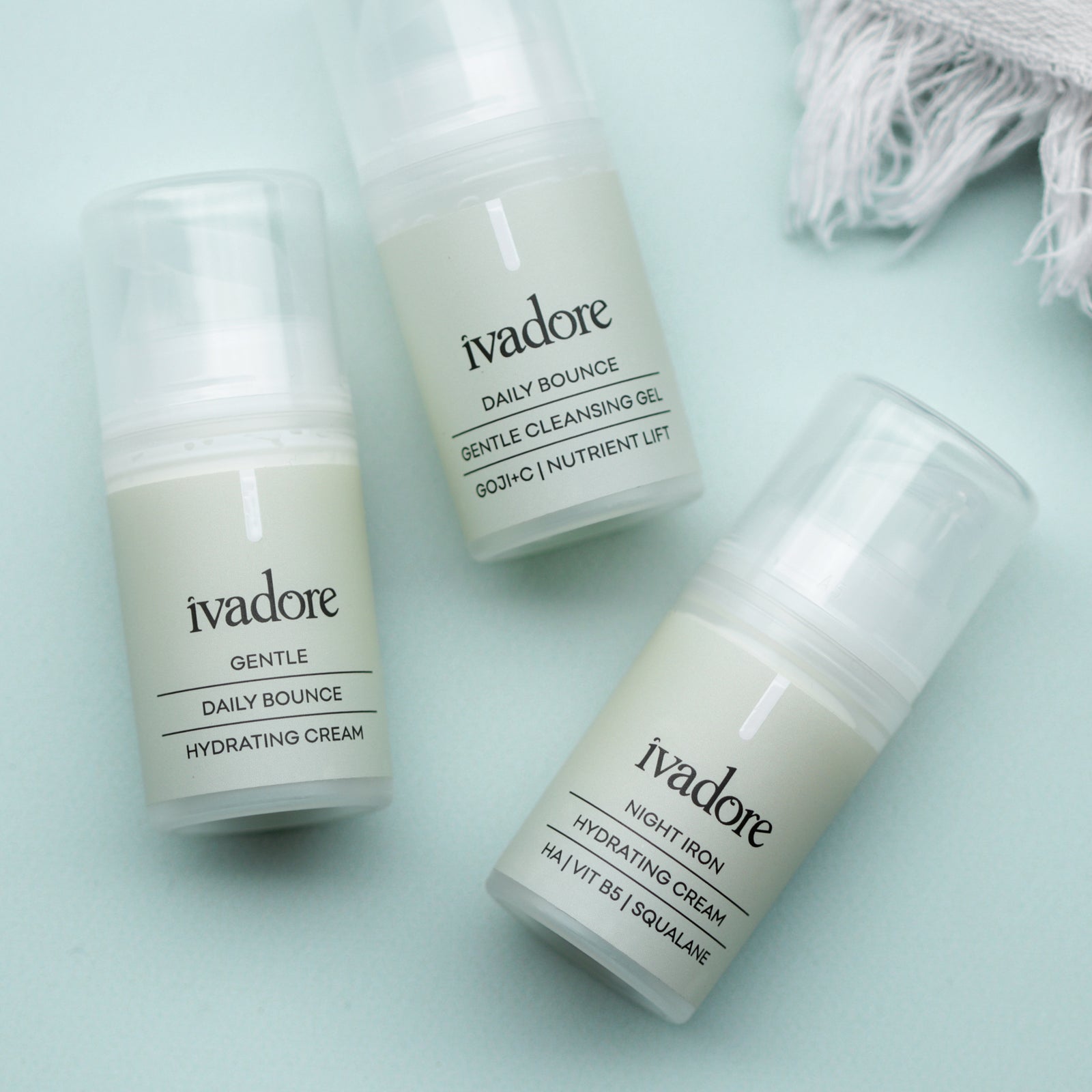 Three 15mL mini bottles laying flat on mint green background showing Ivadore daily bounce hydrating cream, daily bounce cleansing gel and night iron hydrating cream